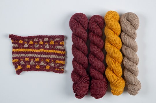 Red, yellow, and brown yarns set beside a sample of the pattern