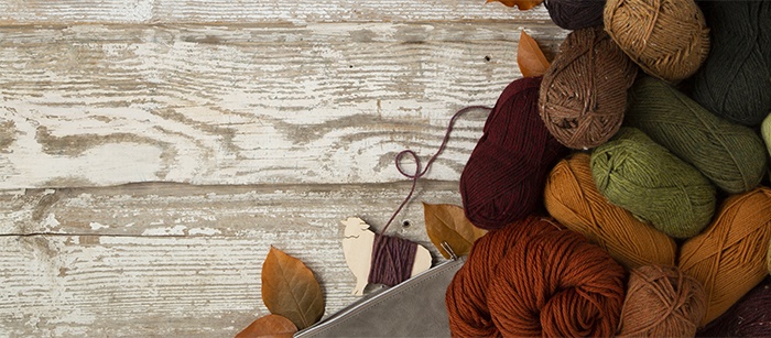 Yarn placed on a wooden table and surrounded by autumn leaves