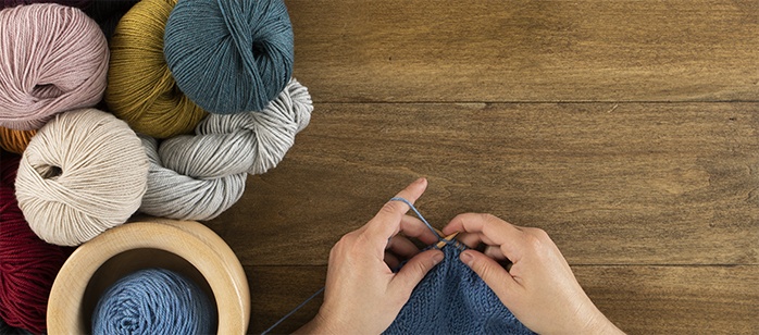 A person knitting with yarn over a wooden table