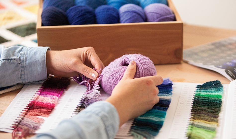 A person compares the purple of a bundle of yarn to the purple sample on a color guide