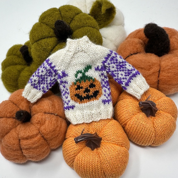 Mini knitted sweater with a jack-o'-lantern on a pile of pumpkins