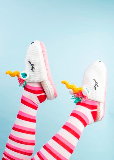 Two feet model a pair of crochet slippers that look like unicorns.